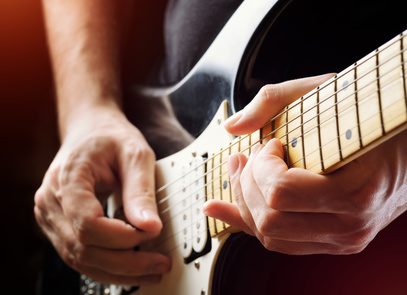 Detailfoto eines auf einer elektrischen Gitarre spielenden Mannes, wie im Gitarrenunterricht