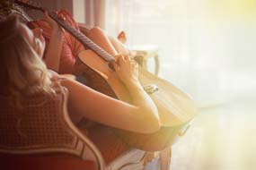 Eine junge Frau sitzt bequem auf einem Stuhl und verbringt die Zeit mit Gitarre üben oder spielen