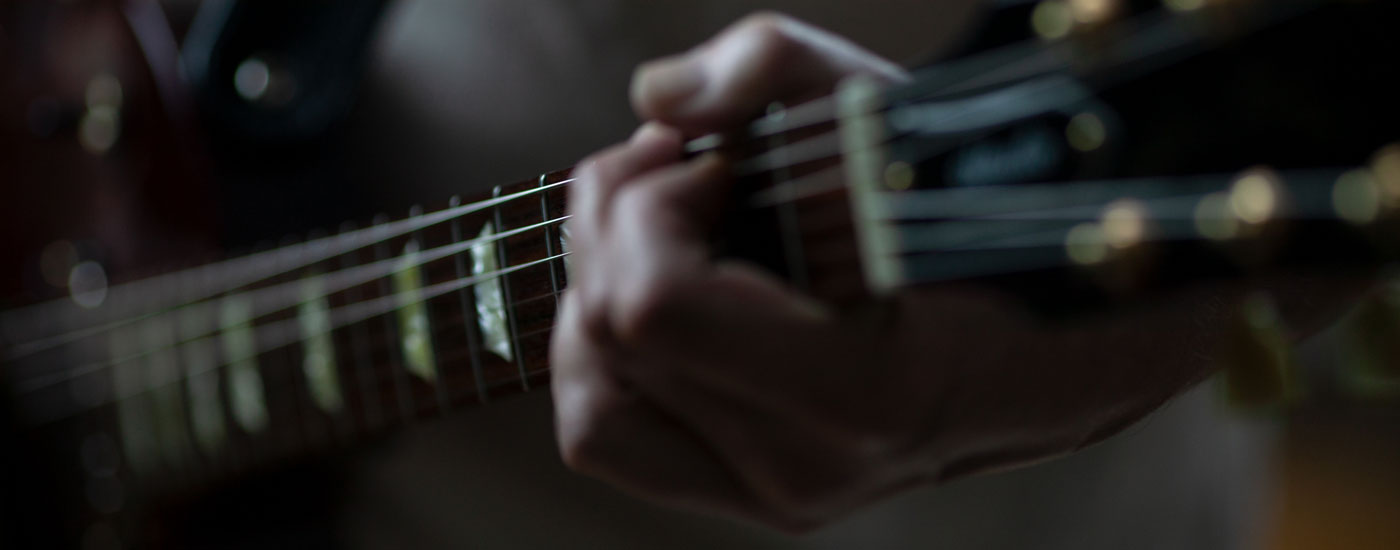 Detailfoto von Gitarrenhals mit Hand, wie im Gitarrenunterricht