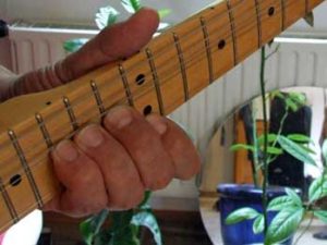 Gitarrenhals mit linker Greifhand, die die Saiten zieht, der Daumen ist schräg nach oben aufgerichtet