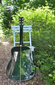Eine Gitarre lehnt an einem hölzernen Klappstuhl in Grünen: Gitarrenunterricht im Freien